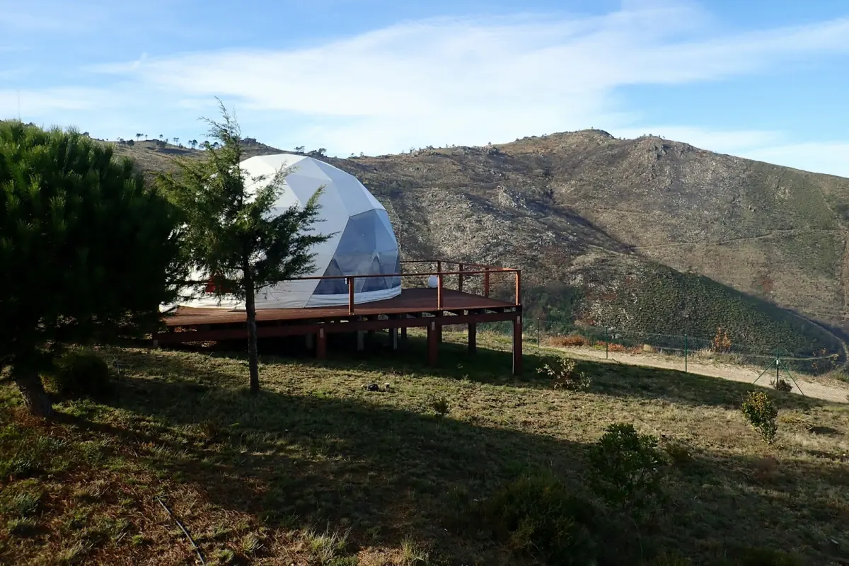 White glamping dome with a wooden deck on a green hillside