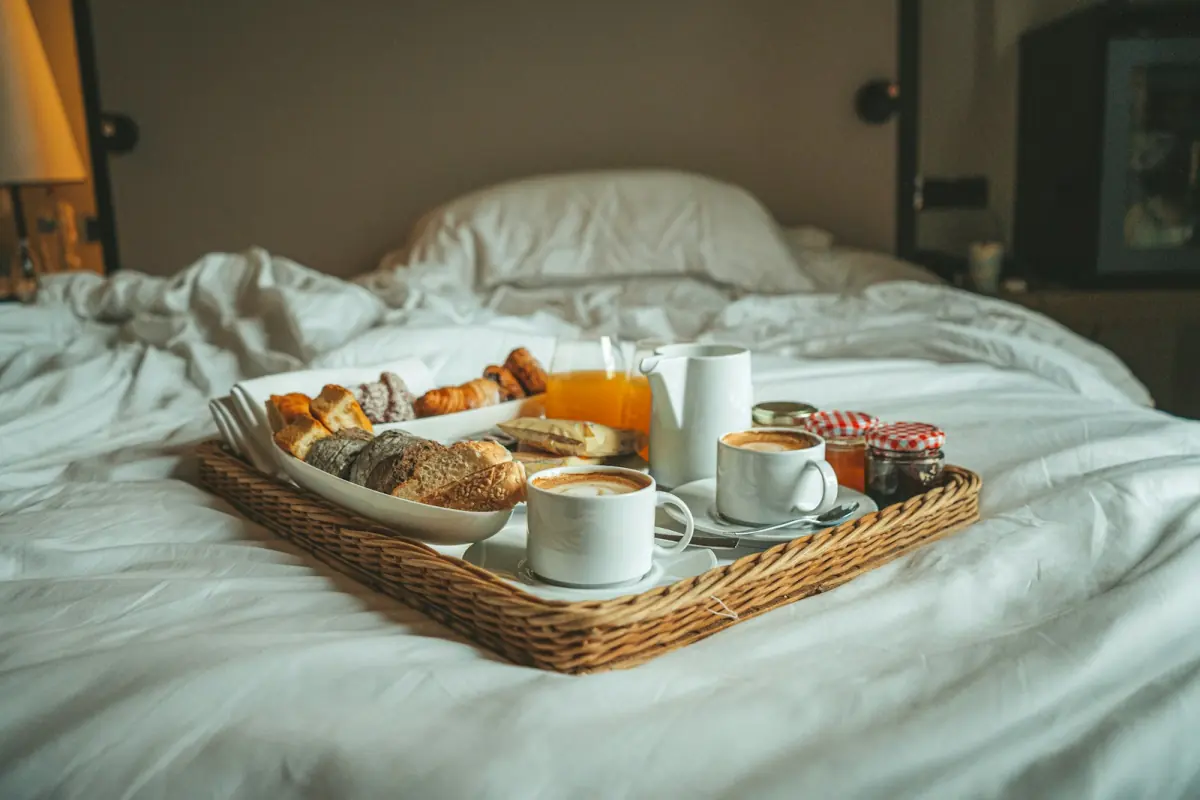 Breakfast tray with coffee and bread on a bed with white sheets